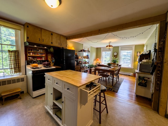 kitchen featuring white gas range oven, a kitchen bar, a center island, white cabinets, and black fridge