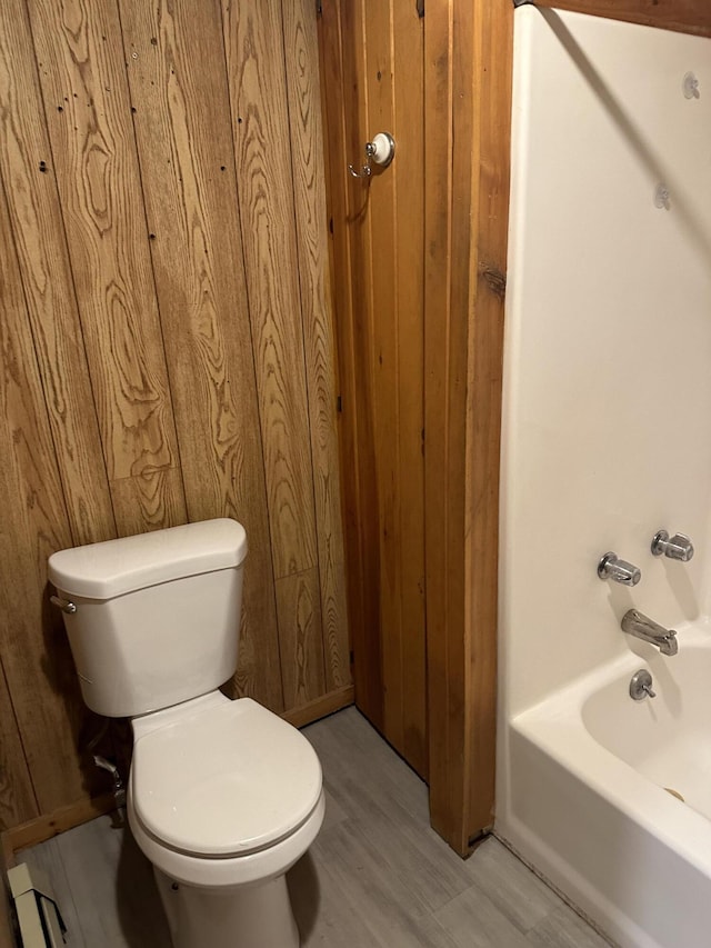 bathroom featuring toilet, wood walls, hardwood / wood-style flooring, and bathtub / shower combination