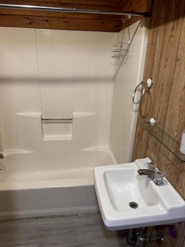 bathroom with shower / bathtub combination, sink, and wood walls