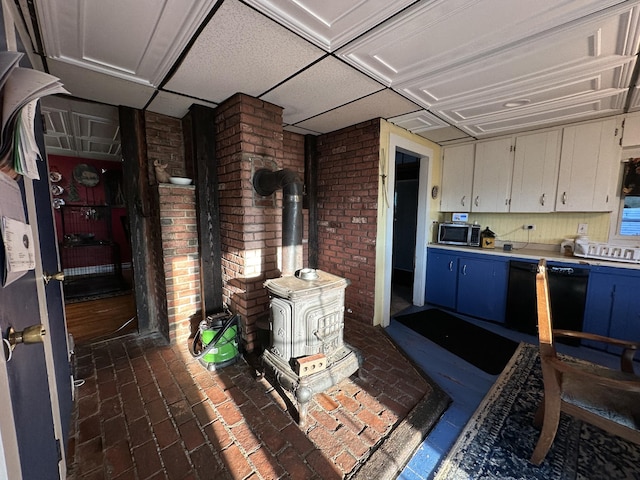 kitchen featuring dishwasher, a drop ceiling, a wood stove, and white cabinets