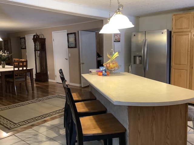 kitchen featuring tile patterned floors, pendant lighting, stainless steel refrigerator with ice dispenser, light brown cabinets, and a breakfast bar area