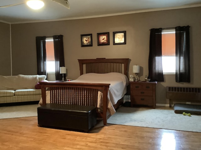 bedroom featuring ceiling fan, radiator, light wood-type flooring, and multiple windows