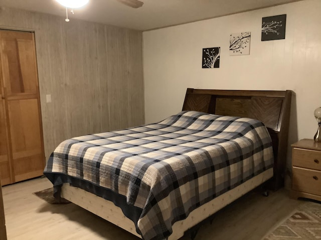 bedroom featuring ceiling fan, light hardwood / wood-style floors, a closet, and wood walls