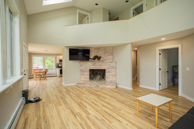 living room with a fireplace, wood-type flooring, a skylight, high vaulted ceiling, and a baseboard radiator