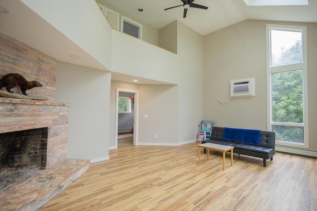 living area featuring light hardwood / wood-style floors, ceiling fan, a high ceiling, a wall mounted air conditioner, and a fireplace