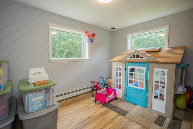 rec room with a baseboard radiator, a wealth of natural light, and wooden walls