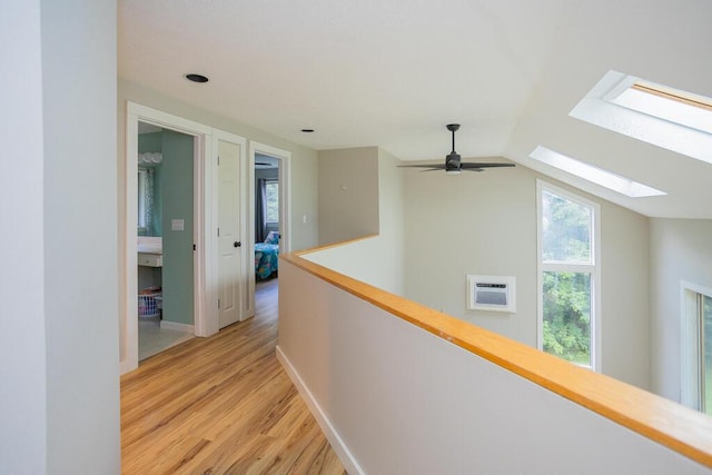 corridor featuring a wealth of natural light, vaulted ceiling with skylight, and light hardwood / wood-style floors