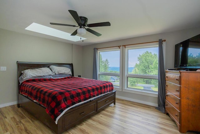 bedroom with ceiling fan, a skylight, and light hardwood / wood-style flooring