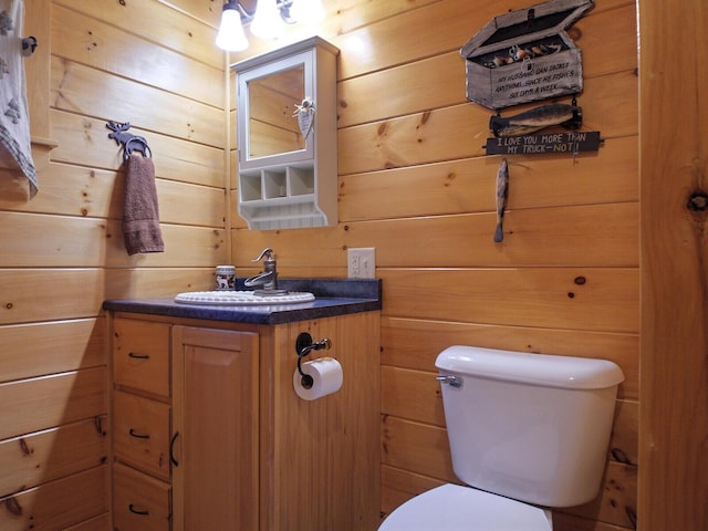 bathroom with vanity, wood walls, and toilet