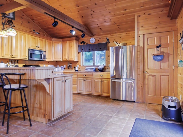 kitchen featuring appliances with stainless steel finishes, rail lighting, decorative light fixtures, vaulted ceiling with beams, and a breakfast bar area