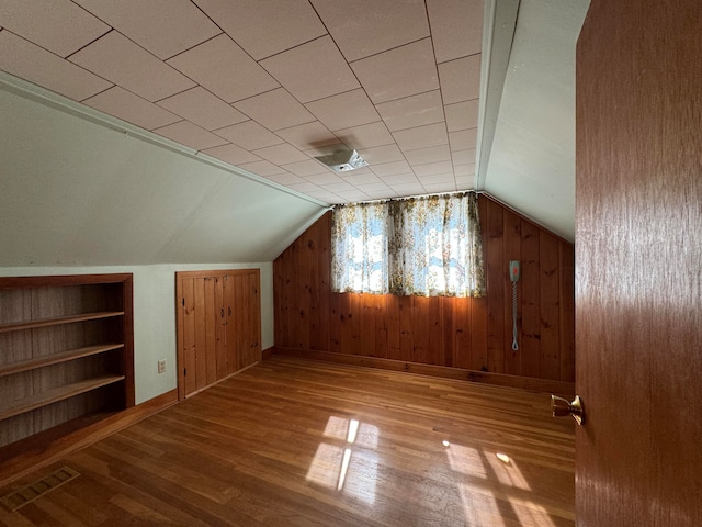 bonus room featuring built in features, wooden walls, lofted ceiling, and light hardwood / wood-style floors