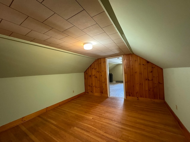 additional living space with wooden walls, a baseboard radiator, hardwood / wood-style floors, and vaulted ceiling