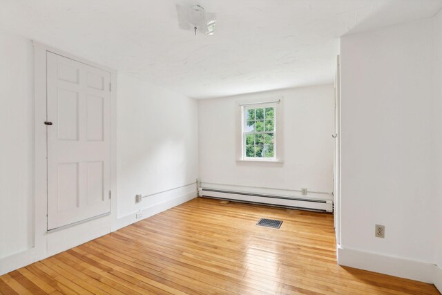 empty room featuring light wood-type flooring and a baseboard heating unit