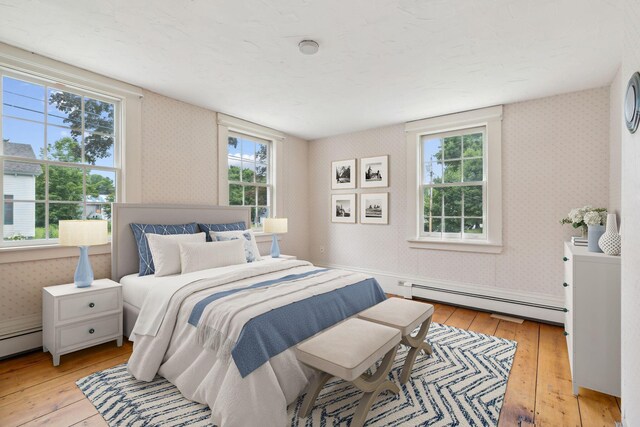 bedroom featuring a baseboard heating unit, light hardwood / wood-style floors, and multiple windows