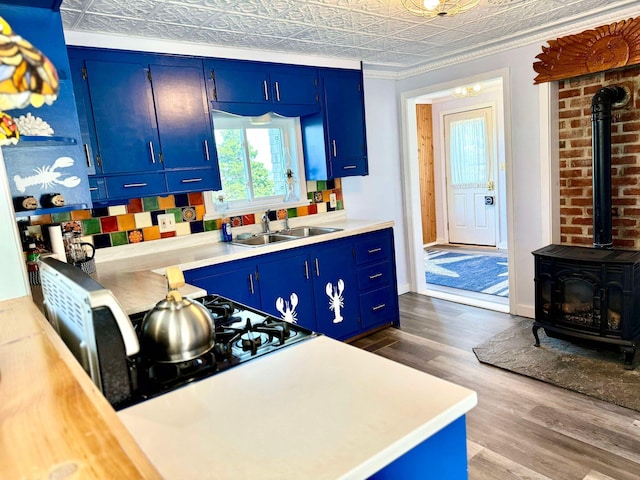 kitchen with hardwood / wood-style flooring, a wood stove, sink, and blue cabinetry