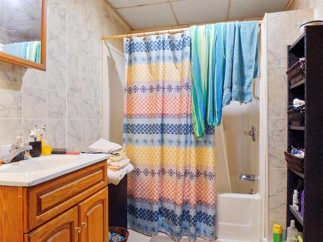 bathroom featuring a paneled ceiling, vanity, shower / bathtub combination with curtain, and tile walls