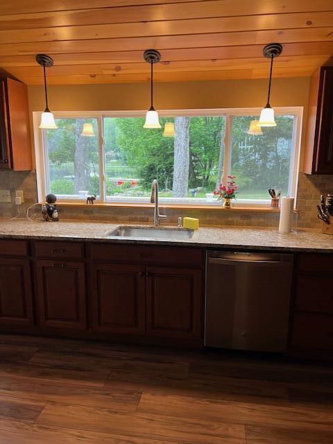 kitchen with pendant lighting, tasteful backsplash, stainless steel dishwasher, a sink, and light stone counters