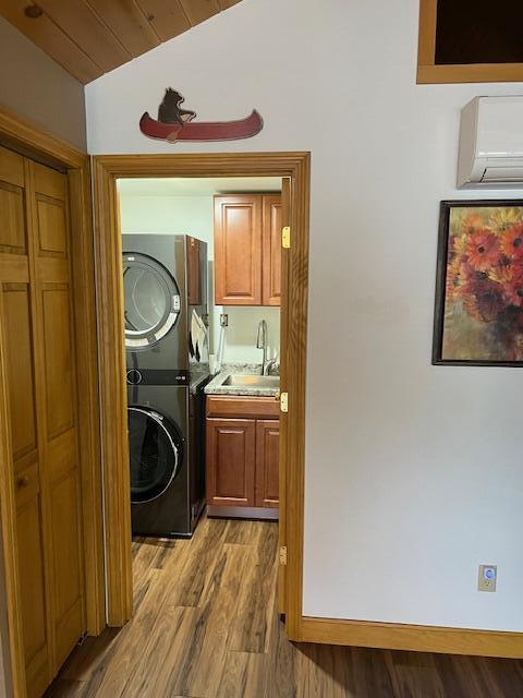 laundry area with a wall mounted air conditioner, cabinet space, a sink, wood finished floors, and stacked washer and clothes dryer