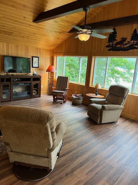 living area featuring wood finished floors, wooden walls, vaulted ceiling with beams, wood ceiling, and a ceiling fan