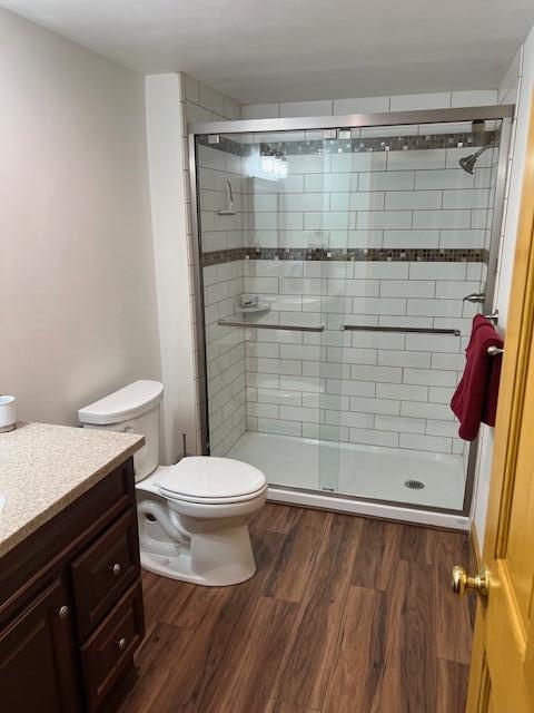 bathroom featuring vanity, a stall shower, wood finished floors, and toilet