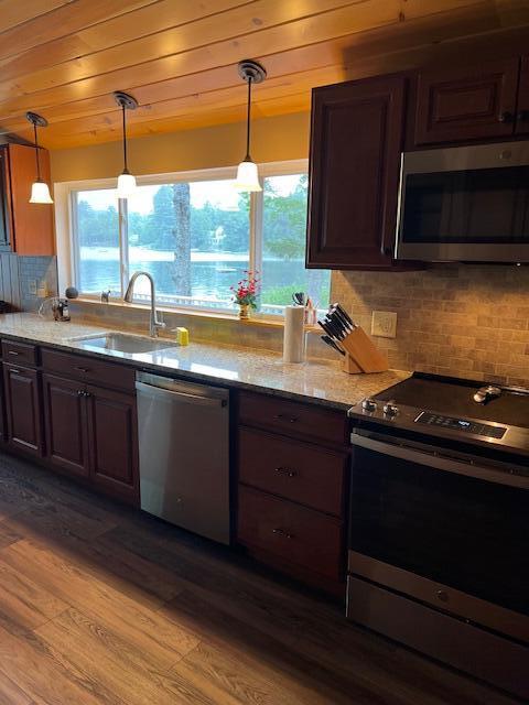 kitchen with light stone countertops, appliances with stainless steel finishes, a sink, tasteful backsplash, and dark wood-type flooring