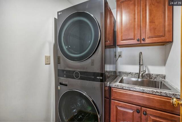 washroom featuring cabinet space, stacked washer / drying machine, and a sink