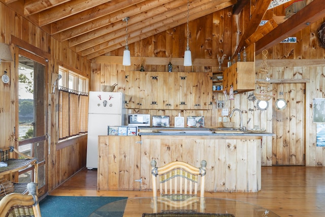 kitchen with wooden walls, decorative light fixtures, lofted ceiling, sink, and white refrigerator