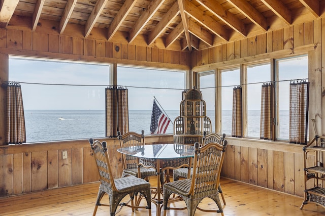 dining space with a water view, wood ceiling, light wood-type flooring, and wood walls