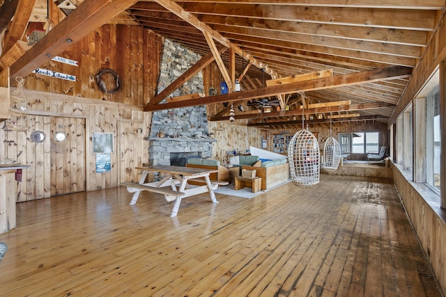 interior space featuring hardwood / wood-style floors, a stone fireplace, high vaulted ceiling, and wood walls