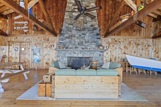 unfurnished living room featuring beamed ceiling, a stone fireplace, hardwood / wood-style floors, and wood walls