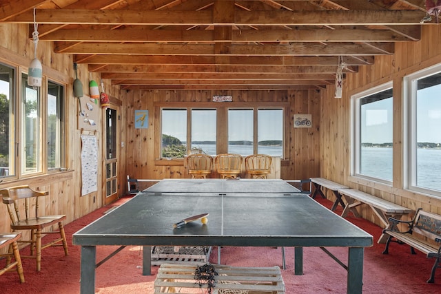 game room featuring a water view, beamed ceiling, and wood walls