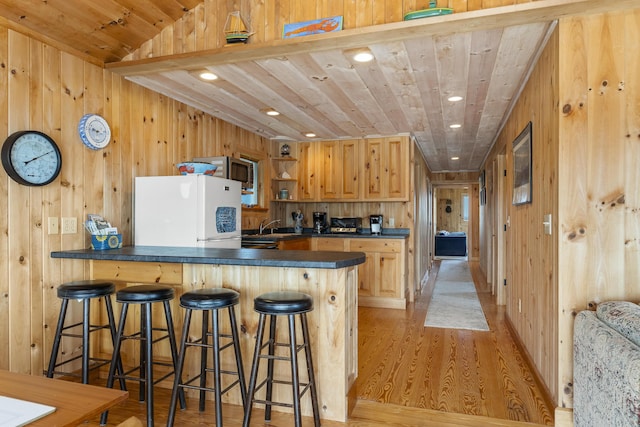 kitchen with a breakfast bar, wooden ceiling, white refrigerator, light brown cabinets, and kitchen peninsula