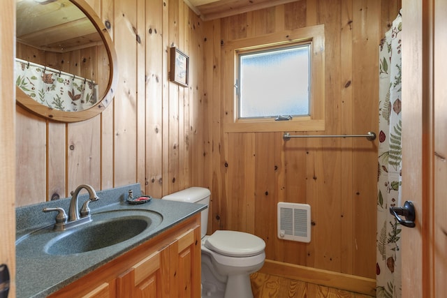 bathroom featuring vanity, toilet, heating unit, and wood walls