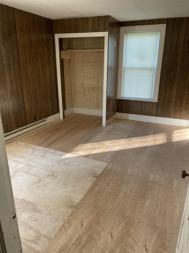 unfurnished bedroom with baseboard heating, a closet, light hardwood / wood-style floors, and wood walls