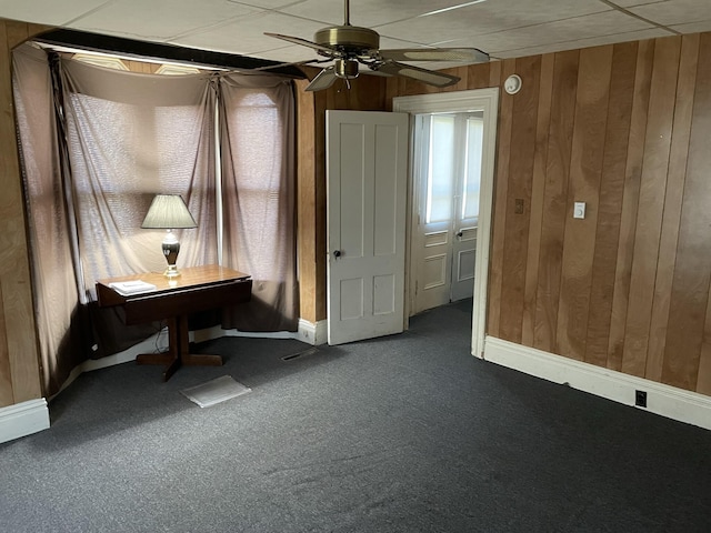 interior space featuring ceiling fan, wooden walls, and dark colored carpet