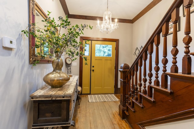 entryway with light hardwood / wood-style flooring, ornamental molding, and an inviting chandelier