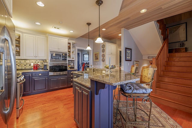 kitchen featuring tasteful backsplash, stone counters, white cabinetry, appliances with stainless steel finishes, and an island with sink