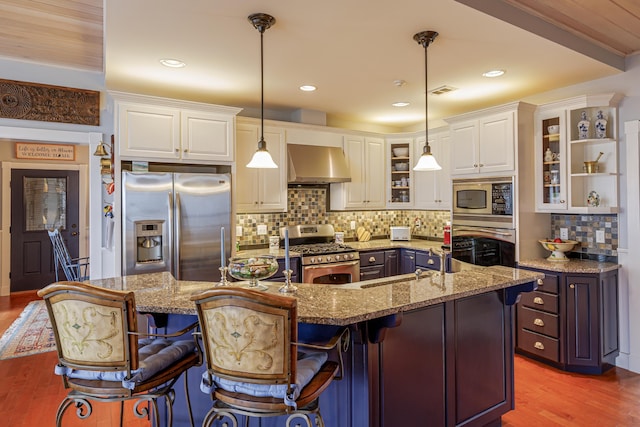 kitchen with a breakfast bar, wall chimney range hood, stainless steel appliances, and hanging light fixtures