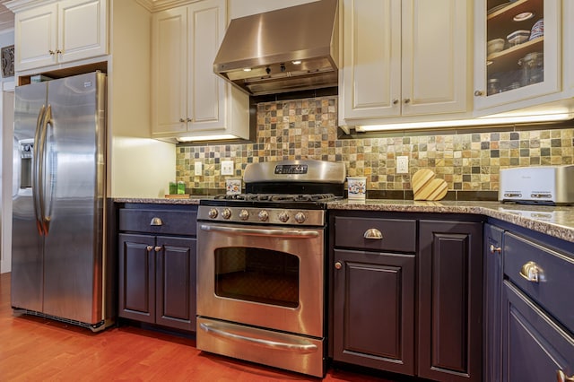 kitchen featuring extractor fan, decorative backsplash, light wood-type flooring, appliances with stainless steel finishes, and dark stone counters