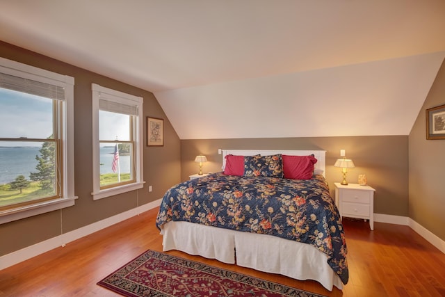 bedroom with lofted ceiling, a water view, and wood-type flooring