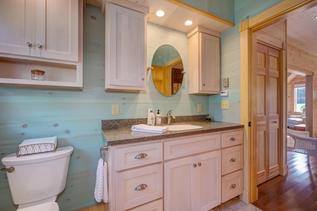 bathroom featuring toilet, wood walls, hardwood / wood-style flooring, and vanity