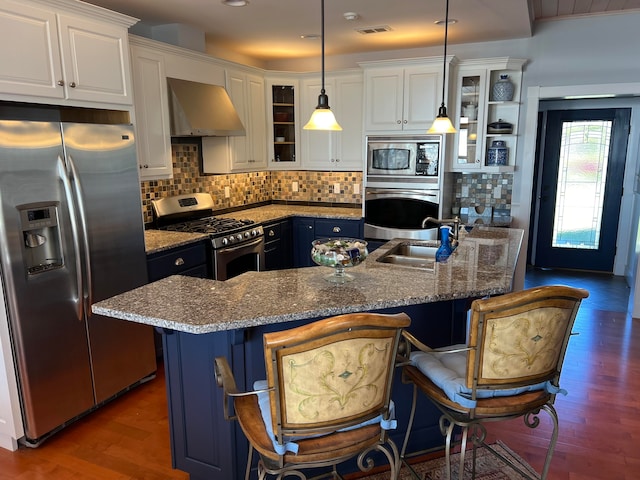 kitchen featuring wall chimney range hood, a breakfast bar, hanging light fixtures, appliances with stainless steel finishes, and white cabinets