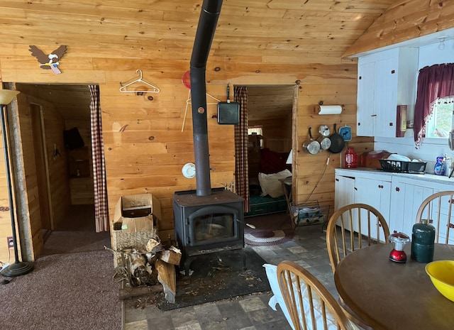 interior space featuring vaulted ceiling, wooden walls, a wood stove, and wooden ceiling