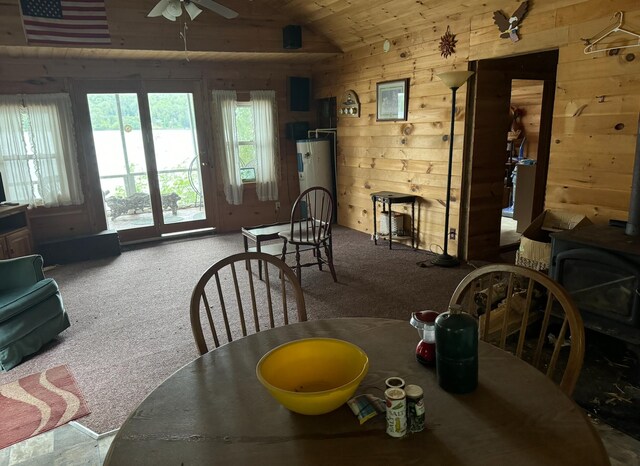 dining room featuring water heater, carpet, a wood stove, and wood walls