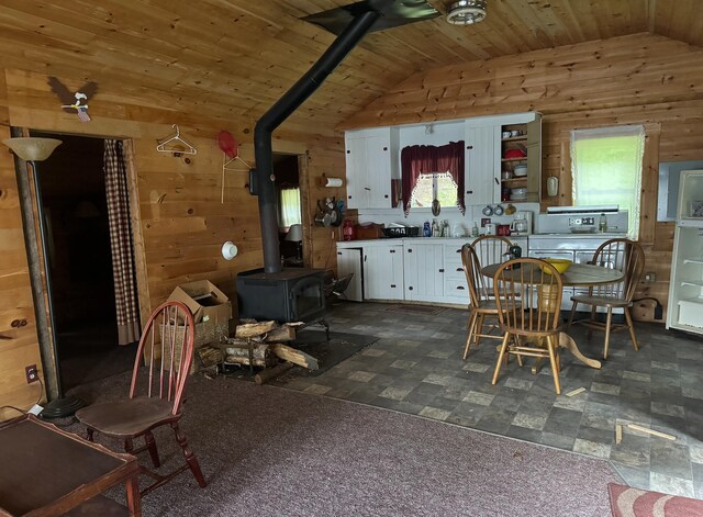 dining area featuring lofted ceiling, wood ceiling, wood walls, and a wood stove