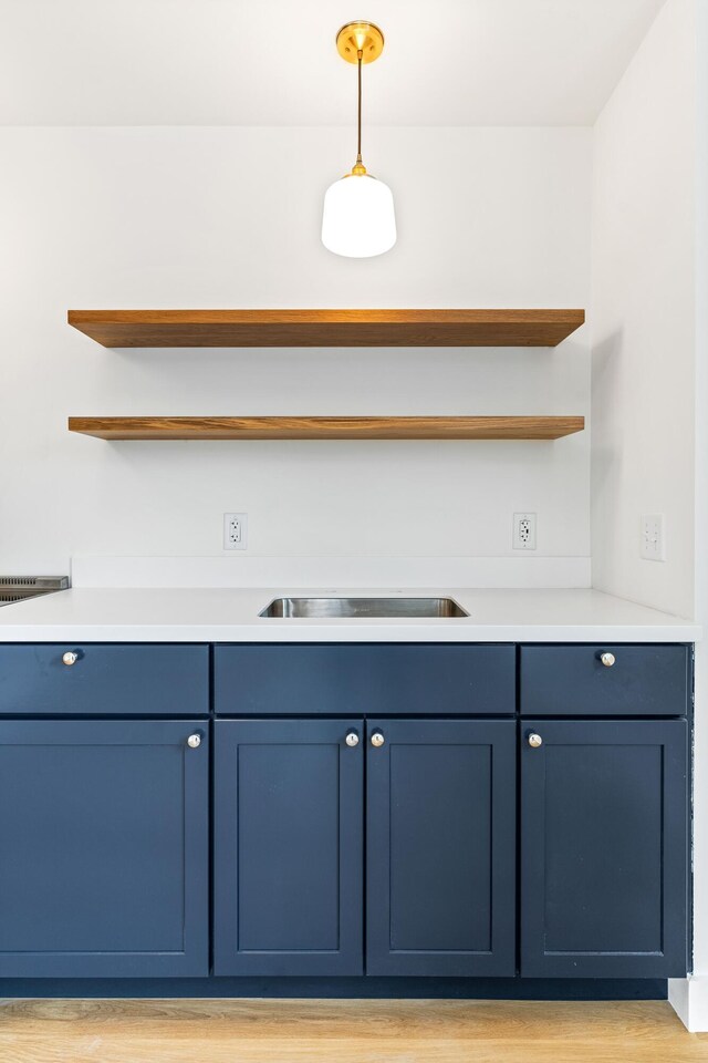 bar featuring light wood-type flooring, hanging light fixtures, sink, and blue cabinetry