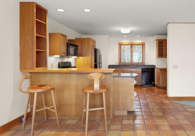 kitchen with black appliances, kitchen peninsula, tile patterned floors, and a kitchen breakfast bar