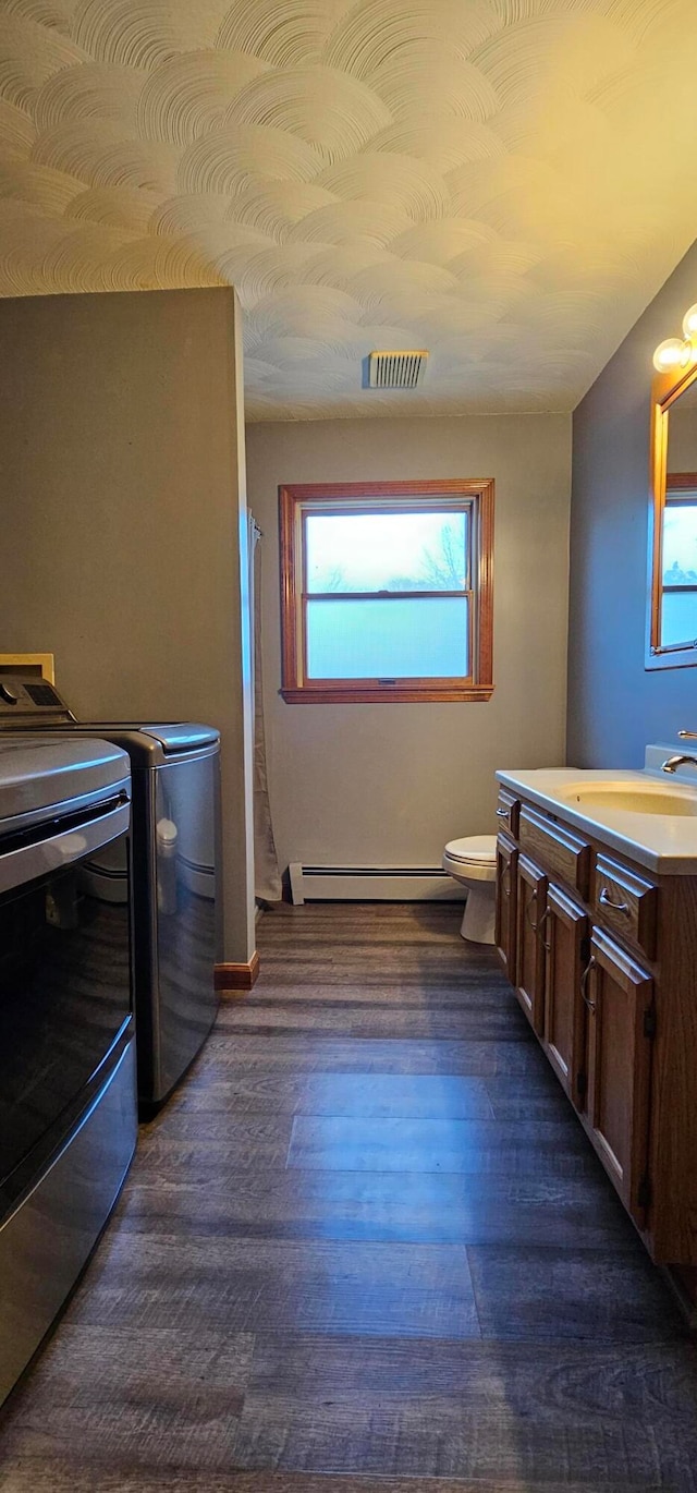 bathroom featuring vanity, toilet, baseboard heating, wood-type flooring, and washing machine and clothes dryer