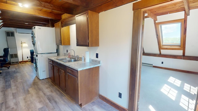 kitchen featuring a baseboard heating unit, stacked washer and dryer, sink, light wood-type flooring, and a wall mounted air conditioner