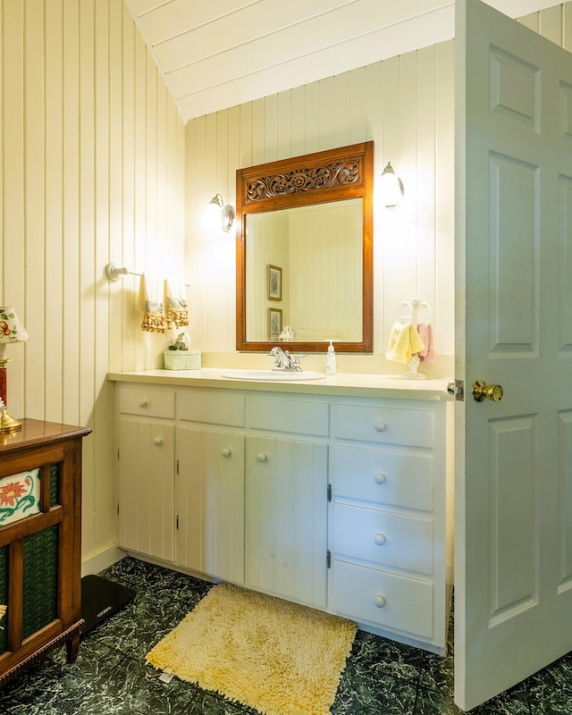 bathroom featuring lofted ceiling, vanity, wooden walls, and tile patterned flooring